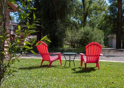 The backside of two empty red chairs in a park with grass and trees.
