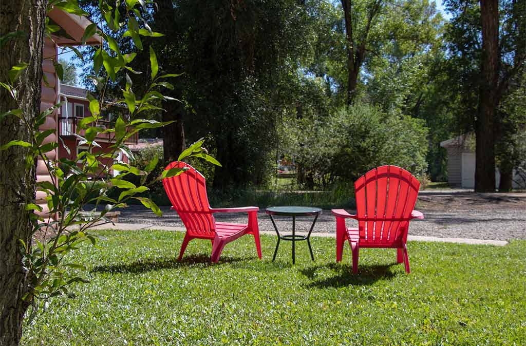 The backside of two empty red chairs in a park with grass and trees.