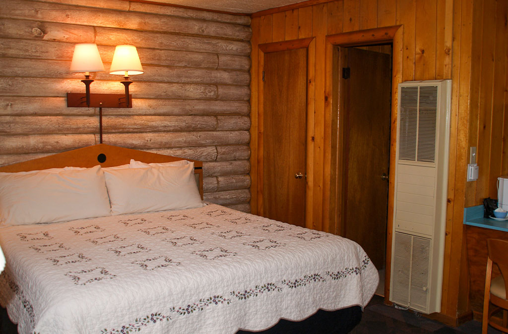 Photo of the Island Acres Resort Motel King Studio Unit with a large clean be in a well lighted log cabin building.
