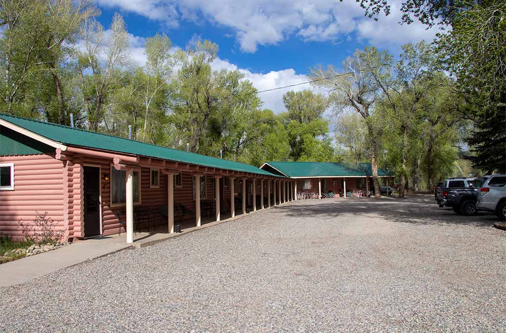 A photo of the Parking Lot and log buildings at Island Acres Resort Motel with cabin buildings in the background