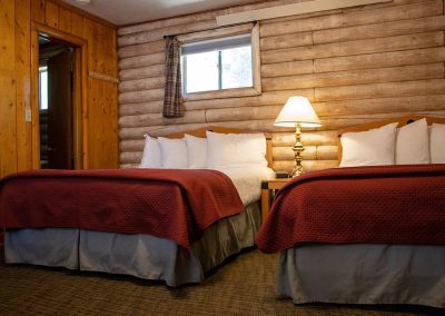 A Queen Studio Unit at Island Acres Resort Motel has two clean beds in a log cabin building.