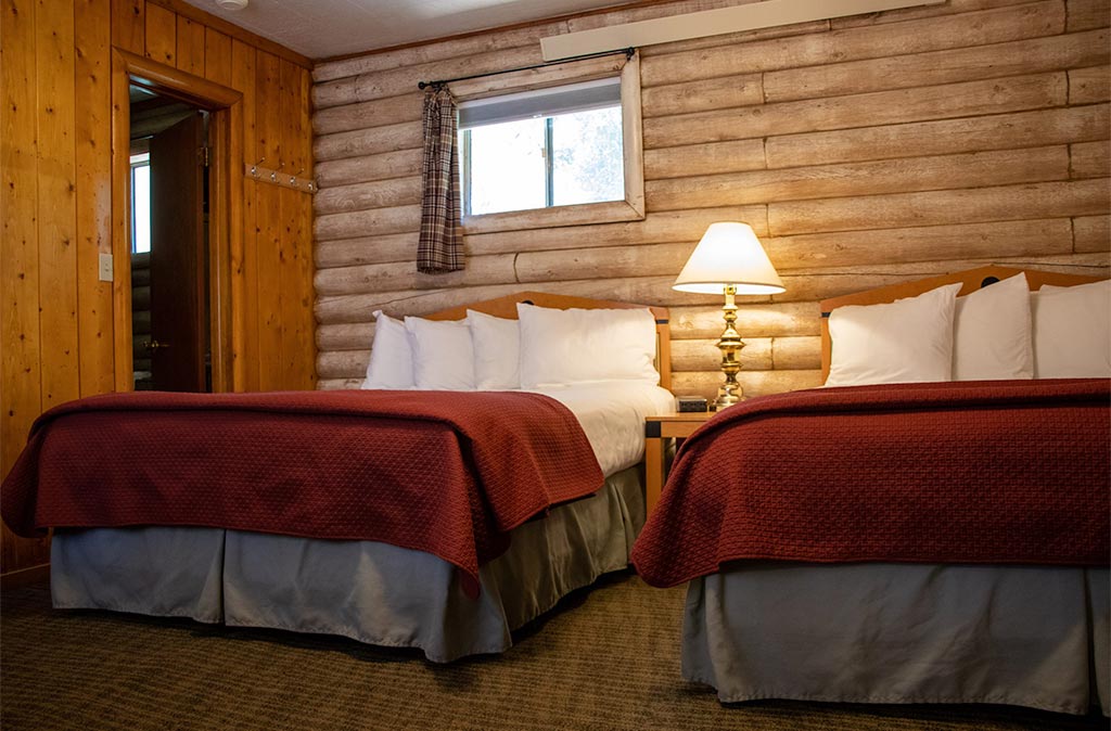 A Queen Studio Unit at Island Acres Resort Motel has two clean beds in a log cabin building.