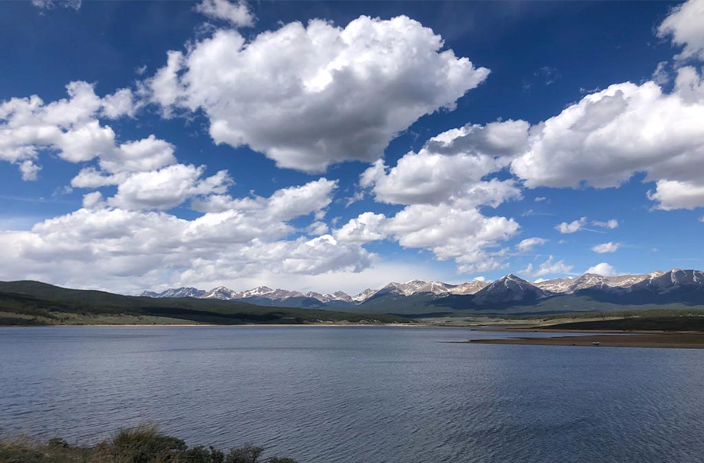 Landscape photo of Taylor Reservoir near Gunnison, Colorado. Still water on the lake on a sunny day with white top mountains in the background.