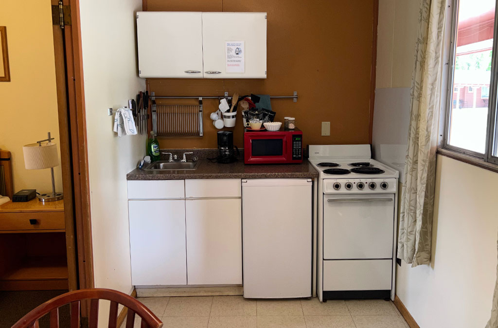 Photo of two-bedroom kitchenette unit at Island Acres Resort Motel showing kitchenette with microwave, sink, mini fridge, stove and oven, and cabinet space.