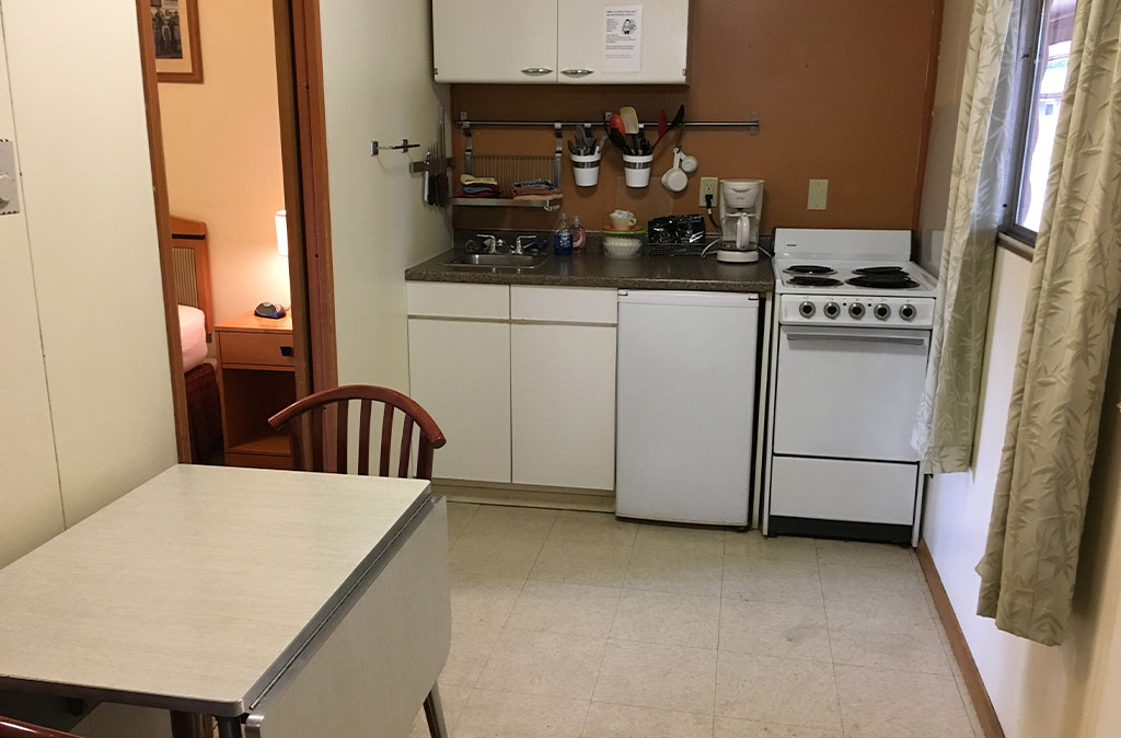 Photo of two-bedroom kitchenette unit at Island Acres Resort Motel showing kitchenette area with a table for two, small stove and oven, mini fridge, and cabinet space.