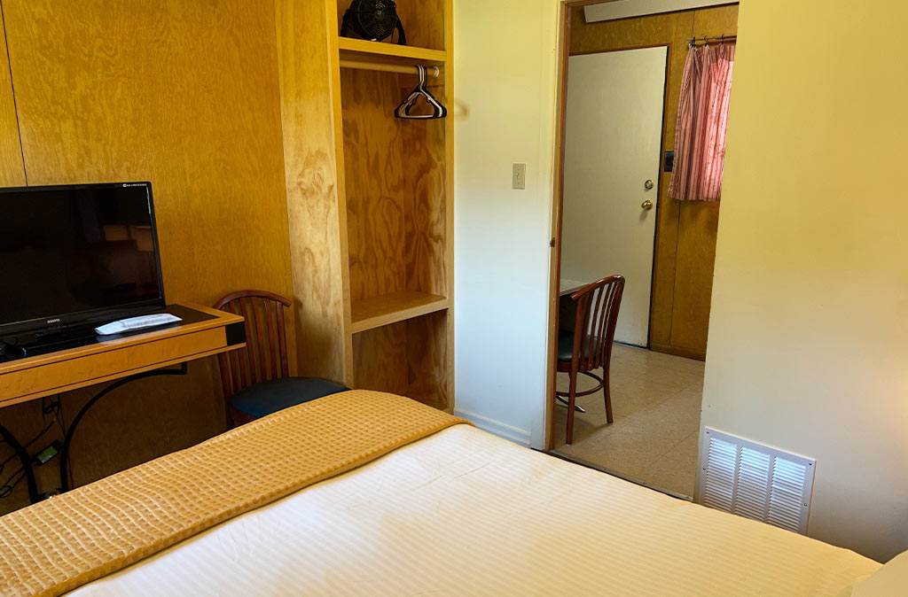 Photo of two-bedroom kitchenette unit at Island Acres Resort Motel showing queen bed and flat screen TV with view of front door to unit walking into kitchenette.