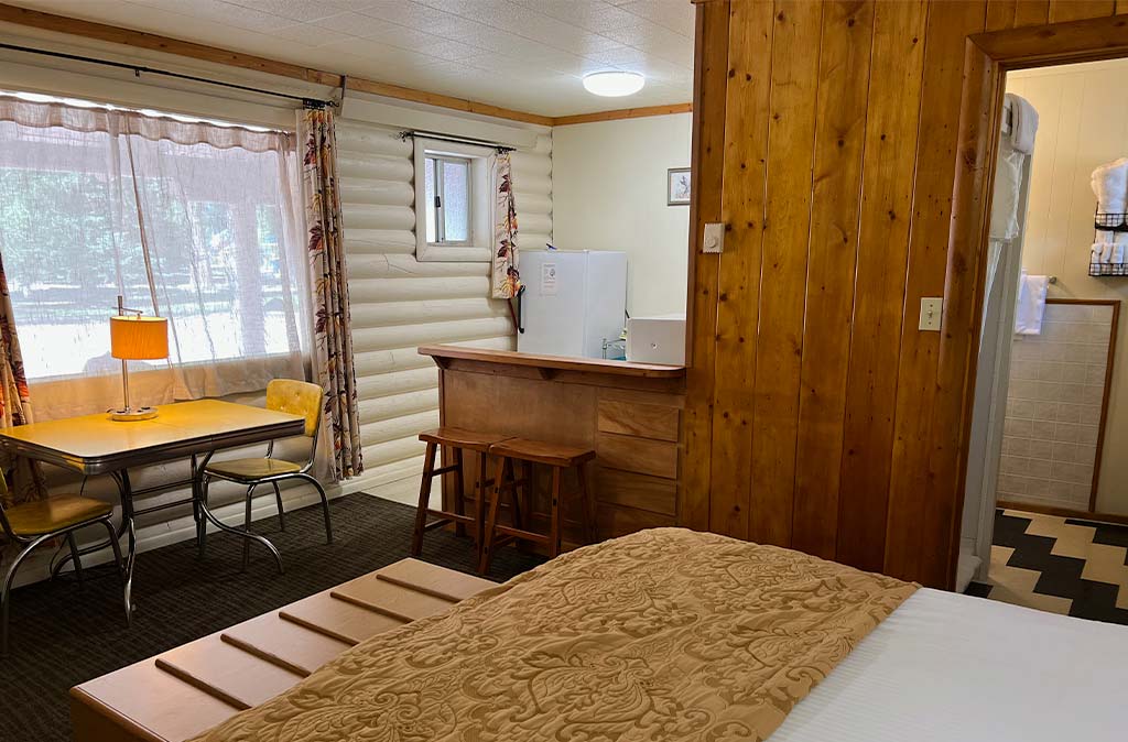 Photo of unit 12 at Island Acres Resort Motel showing dining space on a vintage yellow table, king bed, kitchen and bathroom with vintage tile flooring.