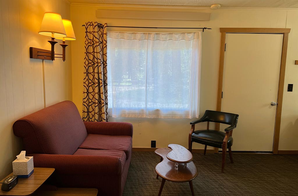 Photo of living room area in Unit 18 at Island Acres Resort motel showing a love seat, funky mid-century coffee table, and a chair.