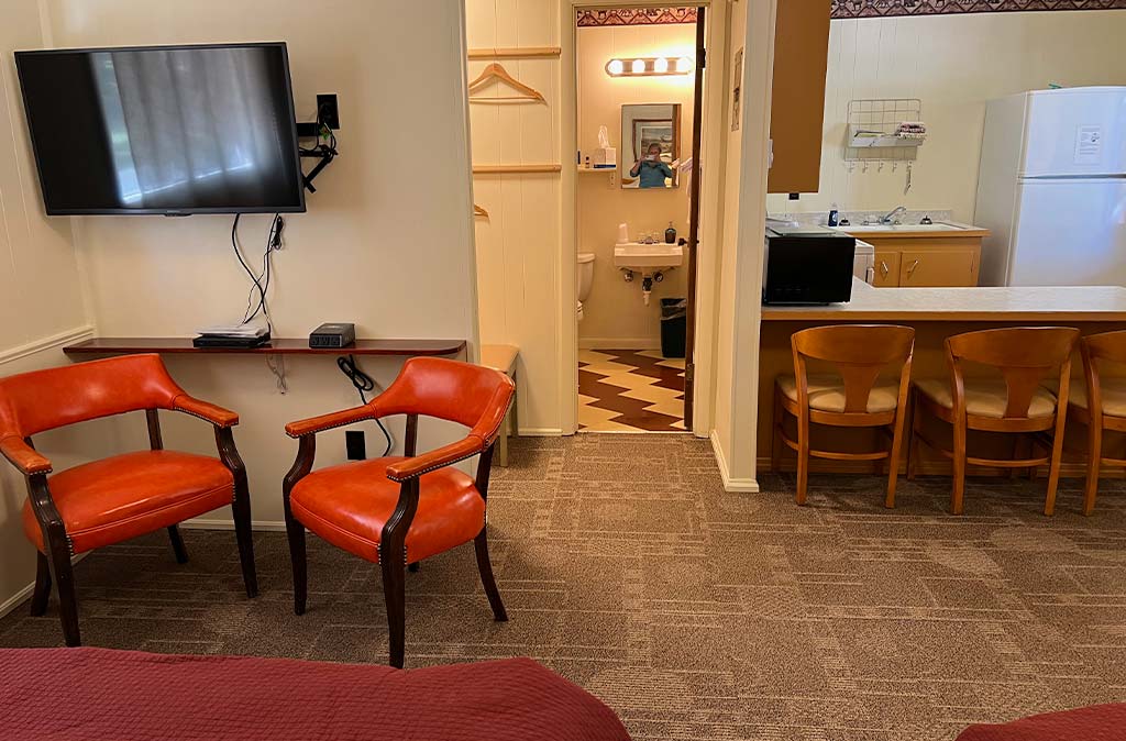 Photo of Deluxe Studio Unit at Island Acres Resort Motel showing seating area, wall-mounted flatscreen TV, kitchen, closet, and bathroom entrance.