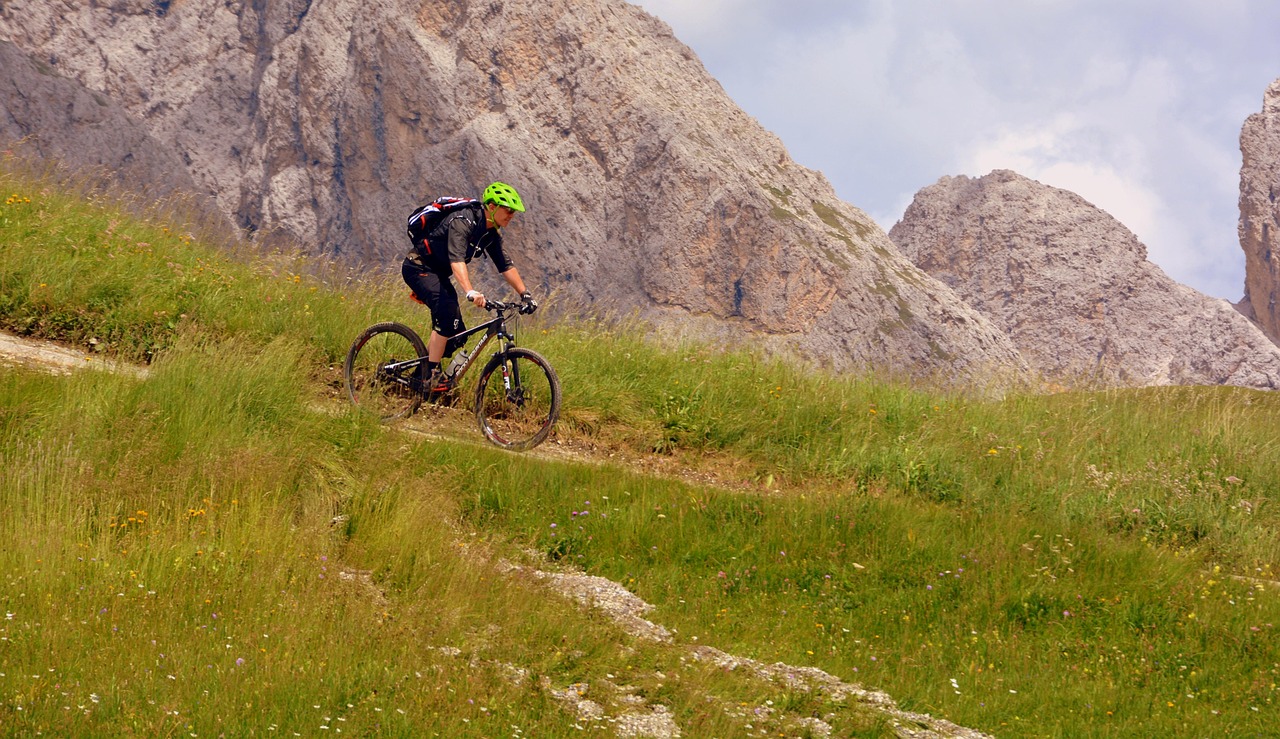 Photo of mountain biker on a train surrounded by green lush mountain meadows and rocky mountains.