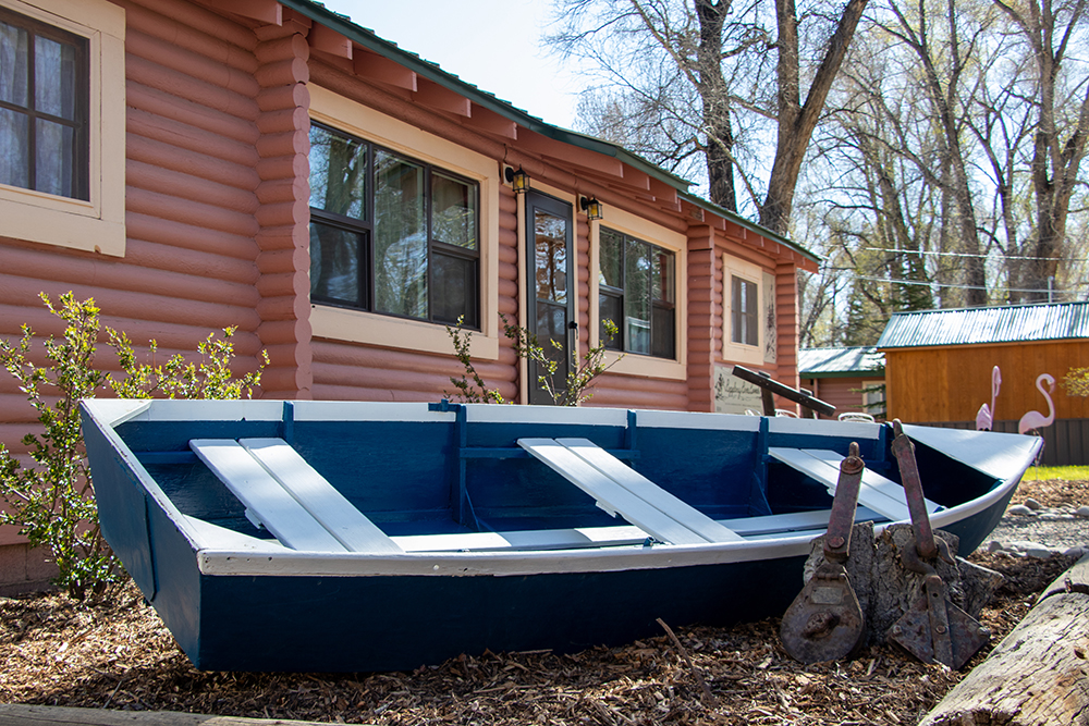 Photo of the historic Rippling River Ranch Cabin at Island Acres Resort in Gunnison, Colorado with a historic Ferry Boat from Iola, Colorado displayed in front.