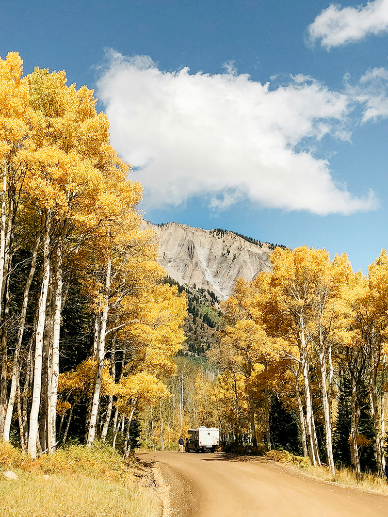 Photo of a car on a dirt road with towering golden aspen and a bald mountain peak in the background for Island Acres Resort blog on the 3 Best Drives for Colorado Leaf Peeping Near Gunnison